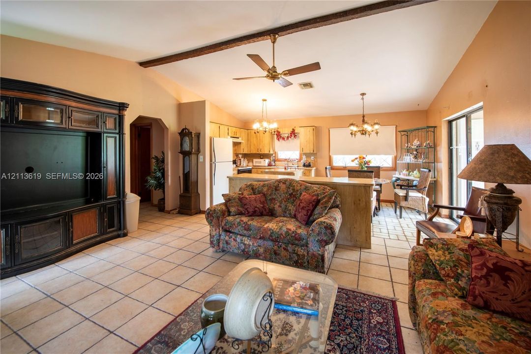 Open-concept interior featuring vaulted ceilings with exposed wood beams, ceramic tile flooring, built-in cabinetry, and a kitchen peninsula