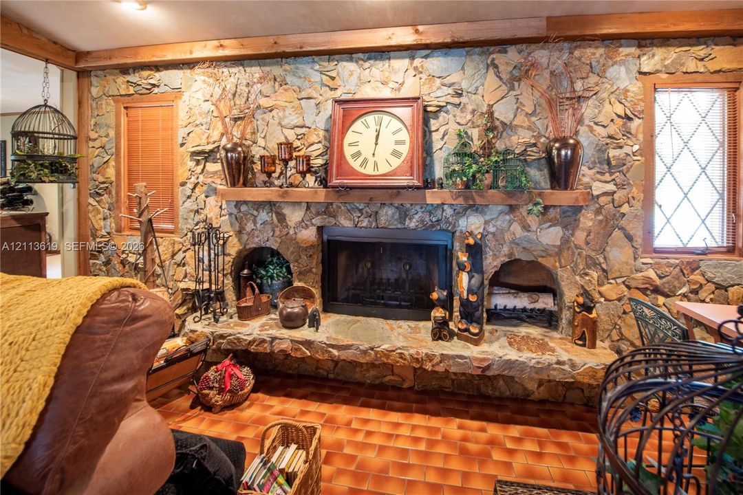 Floor-to-ceiling natural stone fireplace featuring an integrated stone hearth, dual side-arch storage alcoves, a solid timber mantel, and grid-pattern window pane inserts