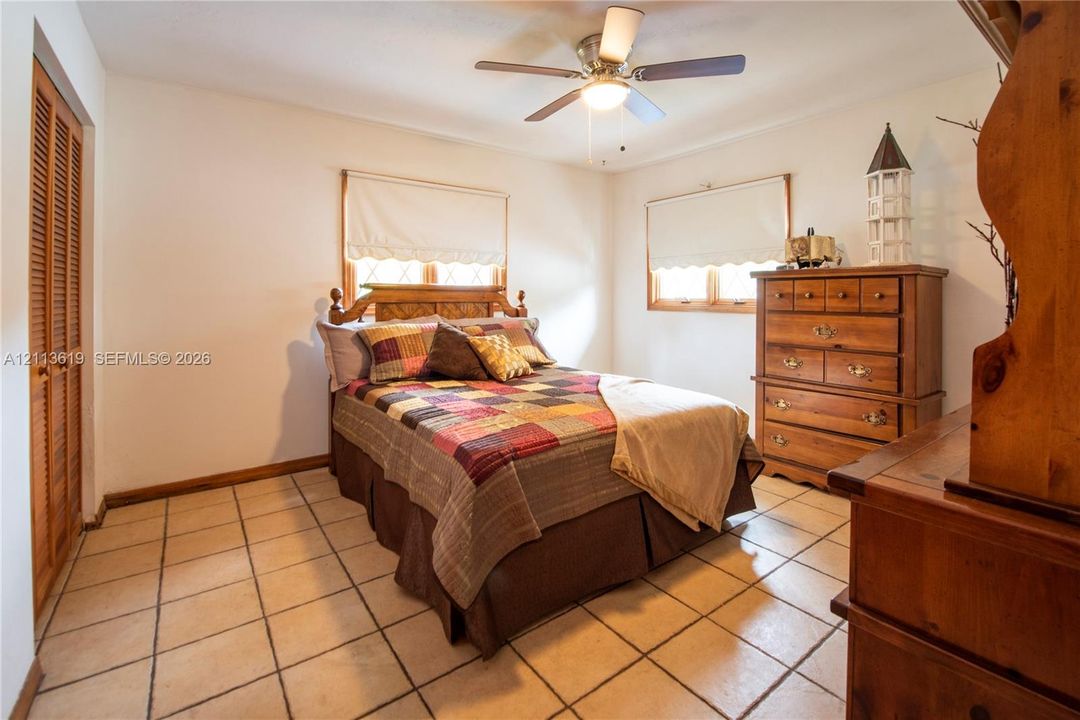 Room featuring neutral walls, square tile flooring, louvered bi-fold closet doors, and a ceiling fan with integrated lighting