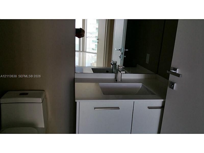 White cabinetry vanity with a light-toned countertop, integrated rectangular sink, polished metal faucet, and wall-mounted mirror