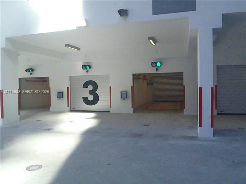 Covered parking area featuring multiple rolling garage doors, concrete flooring, overhead lighting, and digital access control systems