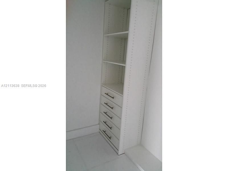 Built-in cabinetry featuring white shelving, five drawers, and metallic hardware