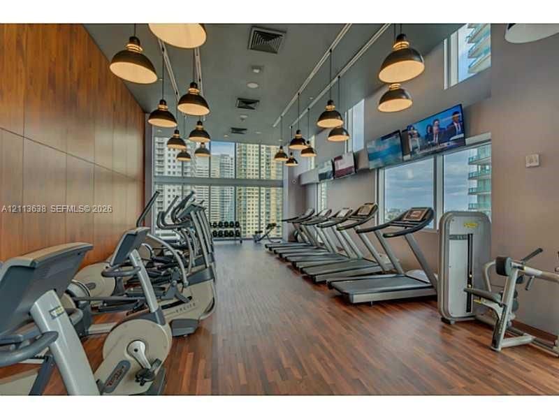 Fitness center featuring wood-finish flooring, floor-to-ceiling windows, polished wood-finish wall paneling, and industrial-style pendant lighting