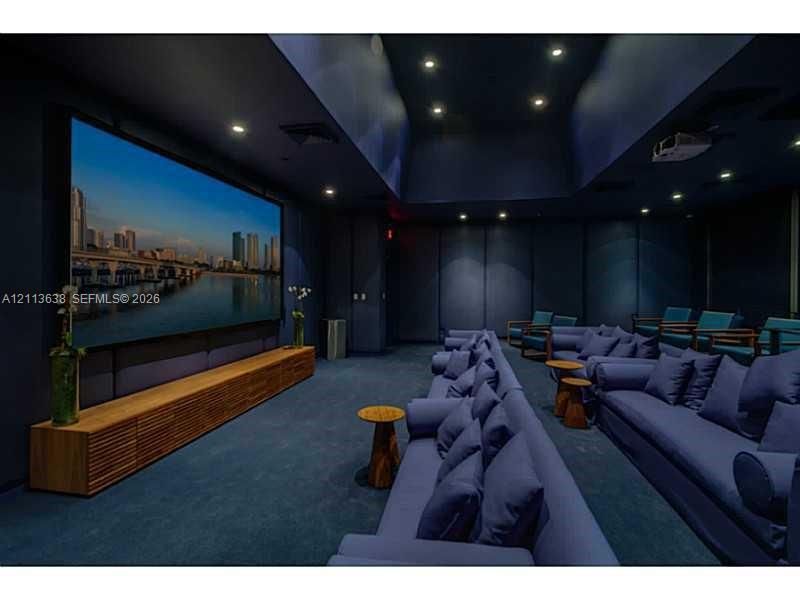 Dedicated media room featuring a large-format projection screen, recessed ceiling lighting, wall-integrated acoustic paneling, and a custom built-in wood-slat cabinetry unit