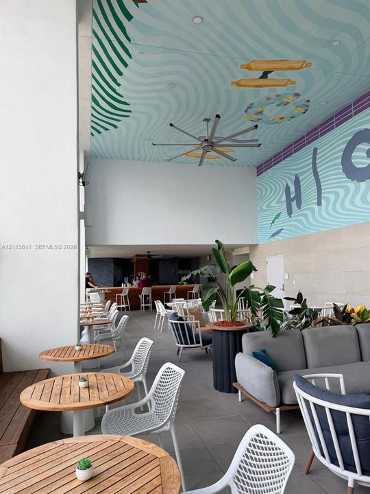 Covered outdoor lounge area featuring a painted mural ceiling, oversized ceiling fan, tile flooring, and integrated bar area