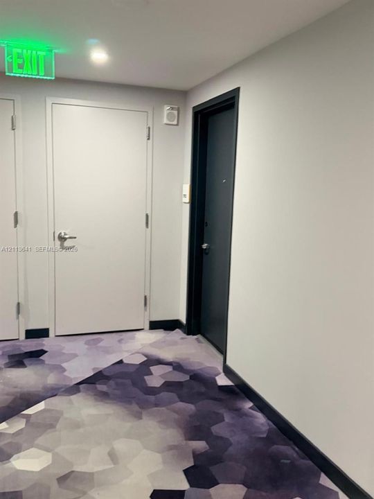 Interior corridor featuring neutral wall finishes, geometric-patterned carpeting, and contrasting door trim