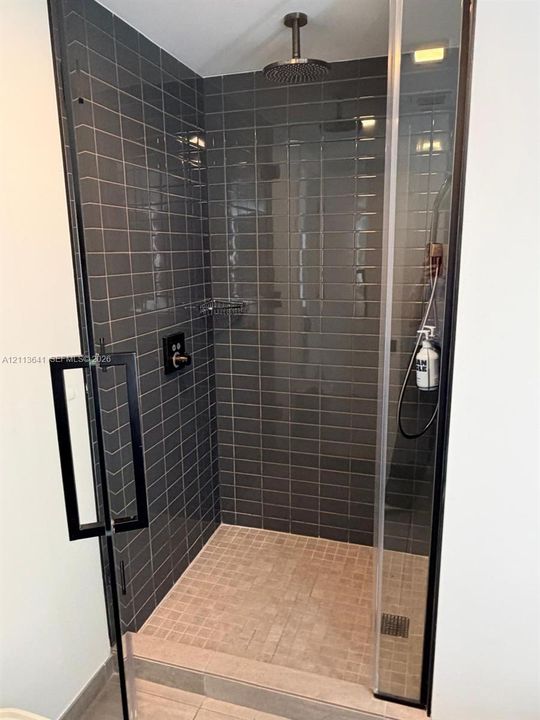 Walk-in shower featuring charcoal subway tile surround, matte black hardware, rainfall showerhead, handheld sprayer, and glass enclosure