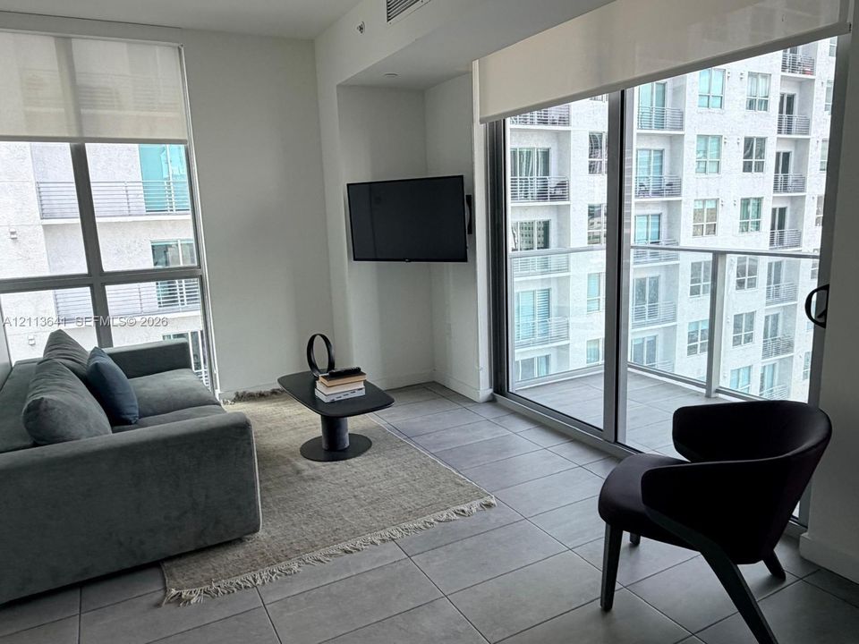 Floor-to-ceiling windows, ceramic tile flooring, private balcony with glass railing, and neutral wall finishes
