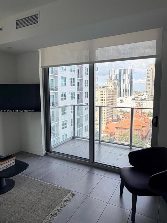 Floor-to-ceiling sliding glass door, private balcony with metal railing, and large-format tile flooring