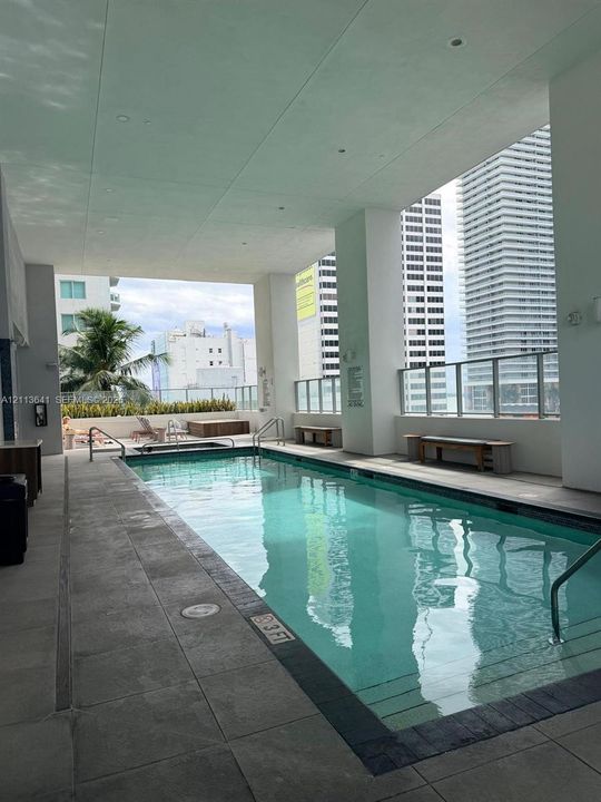 Covered swimming pool featuring tiled decking, built-in bench seating, a glass perimeter railing, and integrated lighting