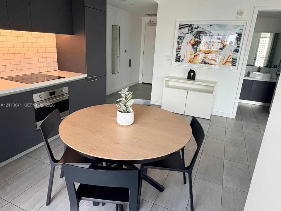 Contemporary kitchen featuring matte charcoal cabinetry, light-toned solid surface countertops, a white subway tile backsplash, and built-in electric oven with a smooth cooktop, complemented by large-format porcelain tile flooring