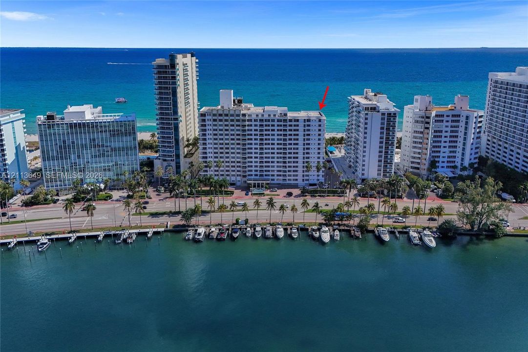 Aerial perspective of multi-story waterfront condominium building featuring immediate ocean frontage, coastal shoreline, and adjacent waterway with dockage