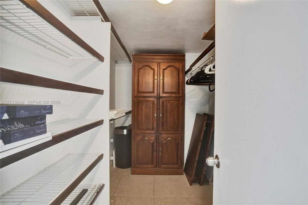 Storage area featuring built-in wood cabinetry, multi-level wire shelving, a hanging rod, and tile flooring