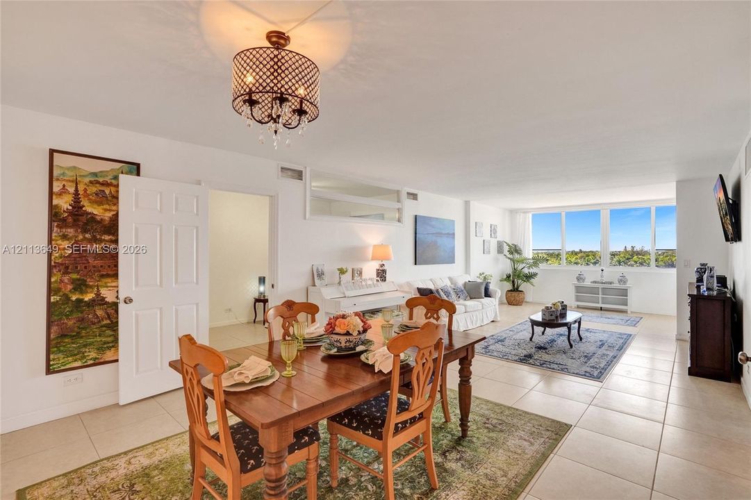 Open-concept floor plan featuring light-colored tile flooring, oversized picture windows, and a decorative drum-style chandelier