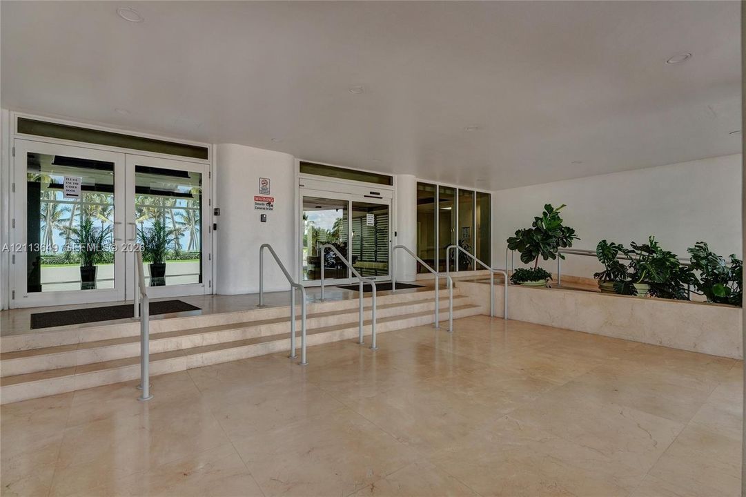 Covered entrance featuring natural stone flooring, tiered steps with metal handrails, floor-to-ceiling glass-paneled doors, and recessed ceiling lighting
