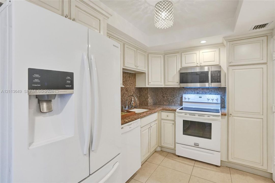 Kitchen featuring off-white cabinetry, stone countertops, integrated stainless steel appliances, tiled flooring, and a decorative pendant light