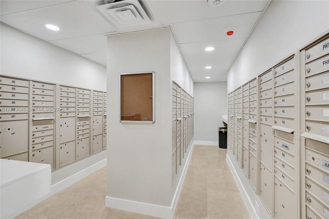 Dedicated mail center featuring secure individual metal compartments, recessed LED lighting, stone-finish flooring, and a wall-mounted display case