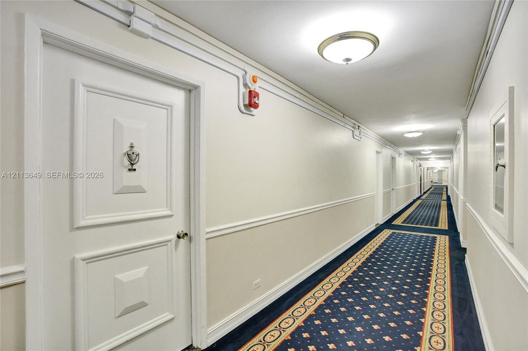 Hallway featuring paneled interior doors with hardware, chair rail molding, wall-mounted flush-mount lighting, and patterned wall-to-wall carpeting