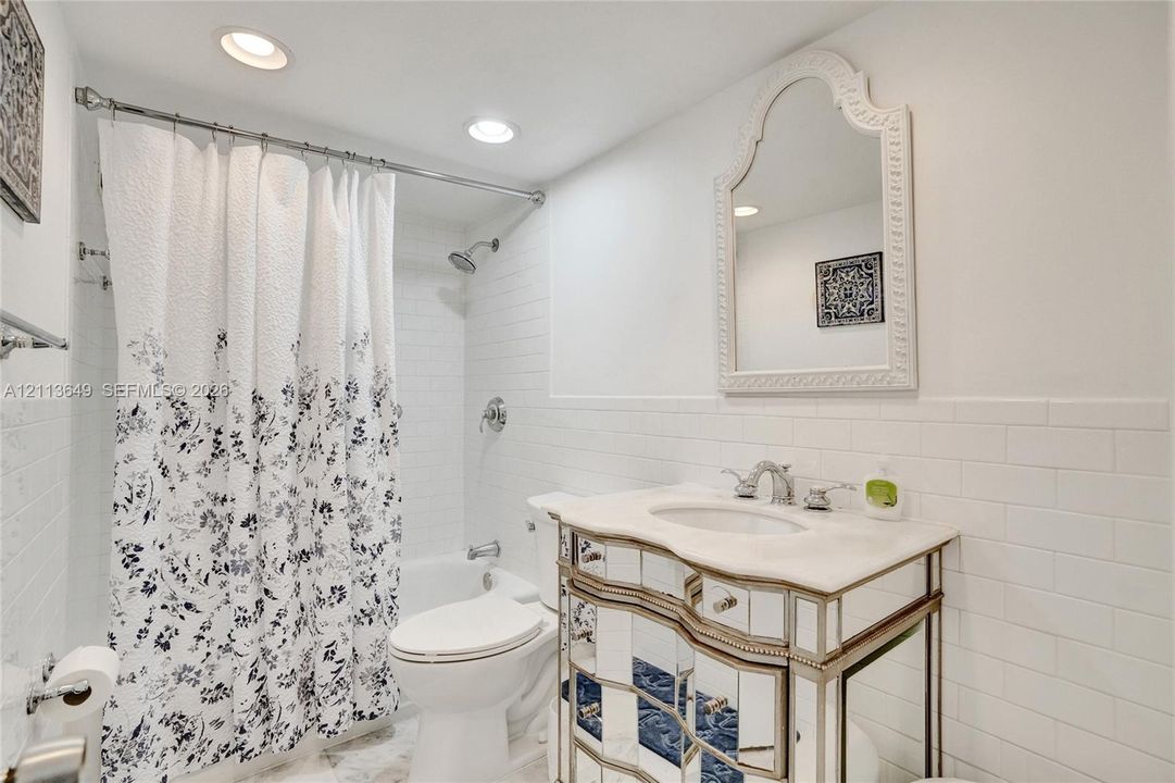 Bathroom featuring a mirrored vanity with a stone countertop, white subway tile wall surround, recessed lighting, and an arched wall mirror