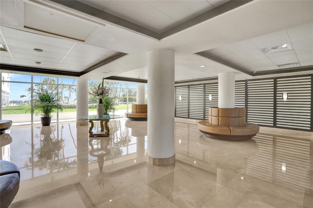 Spacious lobby featuring polished stone flooring, floor-to-ceiling windows, structural columns, and wall-mounted sconces