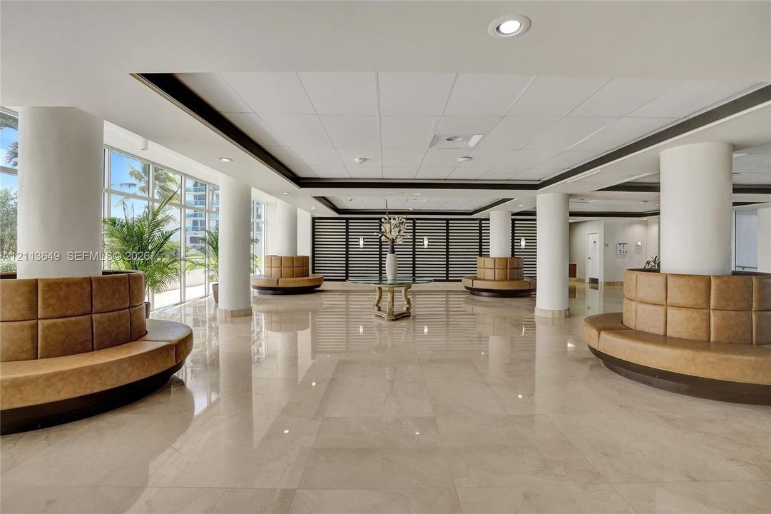 Expansive lobby featuring polished stone flooring, recessed ceiling lighting, floor-to-ceiling windows, and built-in circular seating