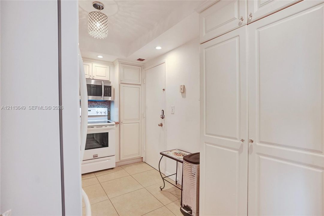 Kitchen featuring white shaker-style cabinetry, stainless steel microwave, stone-finish tile flooring, and a decorative pendant light fixture