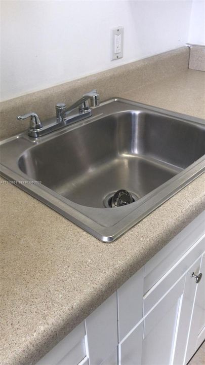 Stainless steel drop-in sink featuring a dual-handle chrome faucet, integrated laminate backsplash, and white cabinetry