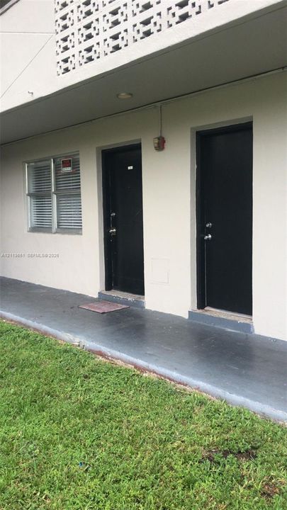 Exterior facade featuring painted concrete walls, decorative breeze block screening, two solid-panel entry doors, and a covered concrete walkway