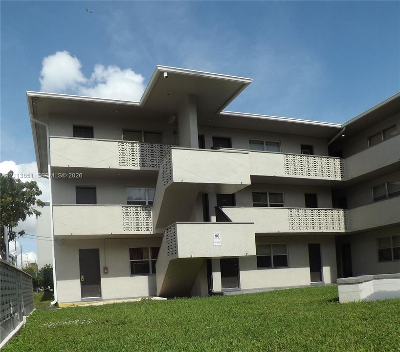 Multi-story exterior featuring smooth stucco siding, decorative lattice balcony railings, and a flat roofline