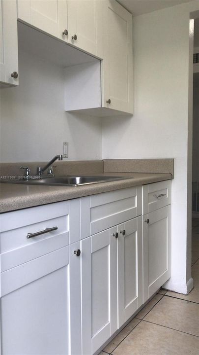 White shaker-style cabinetry, solid-surface countertops, stainless steel sink with a dual-handle faucet, and ceramic tile flooring
