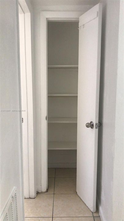 Built-in storage closet featuring five tiered shelves, a single-panel door, and polished metal hardware, set against light-toned tile flooring