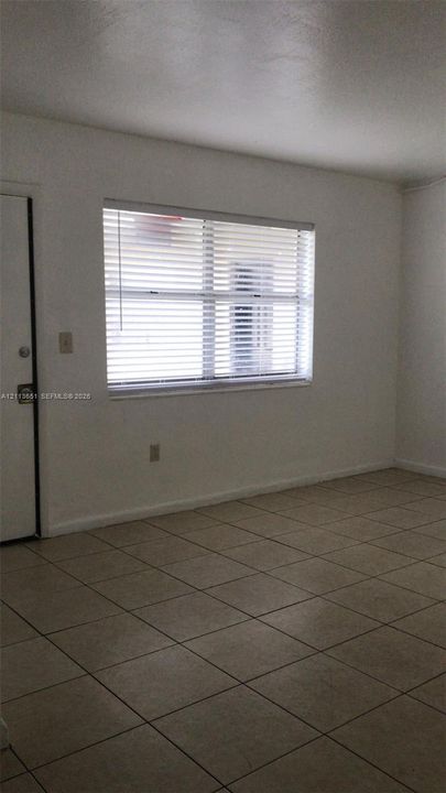 Neutral-toned tile flooring, white wall finishes, and a single-pane window with horizontal blinds