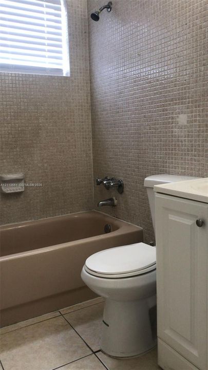 Bathroom featuring floor-to-ceiling mosaic tile walls, a porcelain soaking tub, a white cabinet vanity, and tile flooring