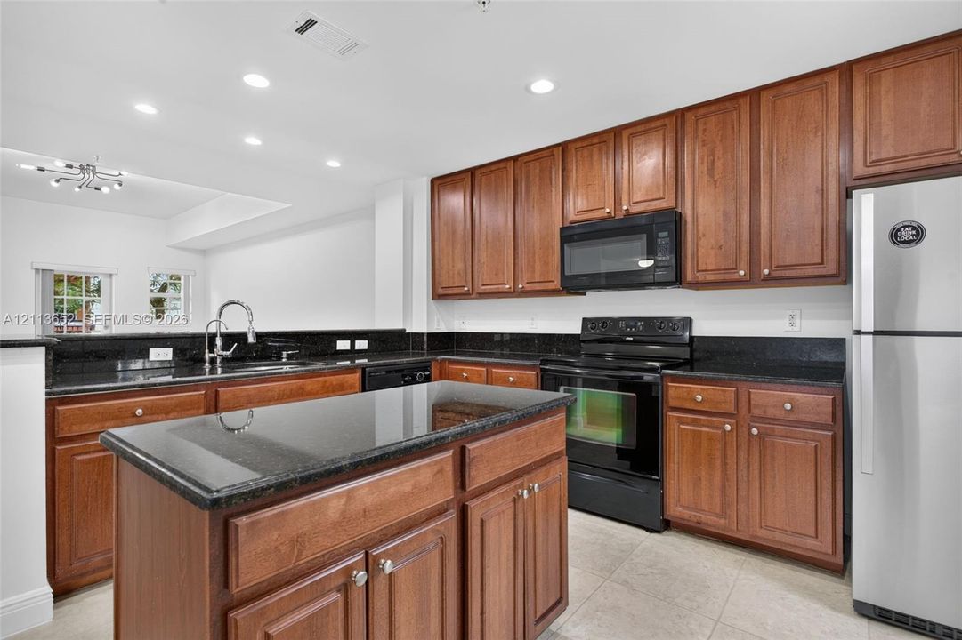 Kitchen featuring dark stone countertops, natural wood-finish cabinetry, center island, stainless steel refrigerator, and recessed lighting