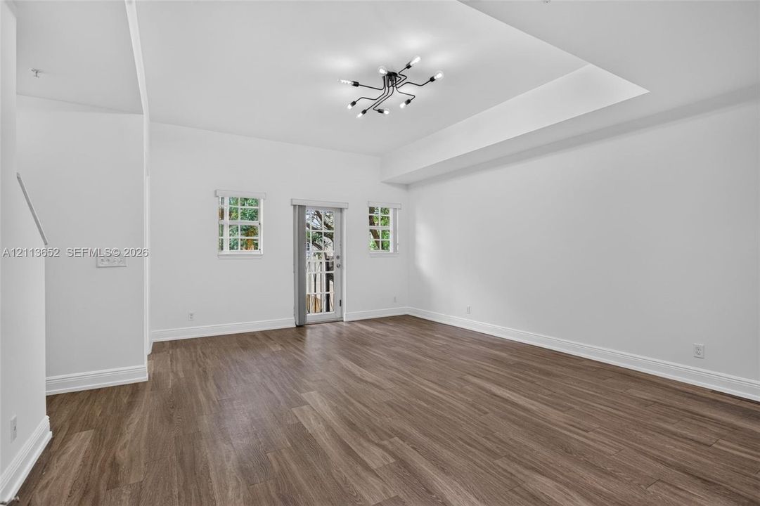 Tray ceiling, wood-finish flooring, multi-light geometric chandelier, and divided light exterior door