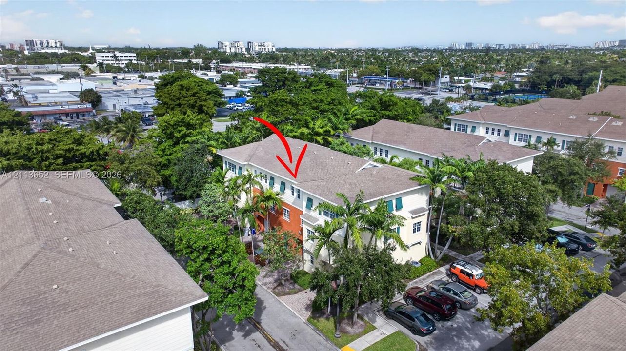 Multi-story residential building featuring a shingled roof, stucco exterior, shuttered windows, and mature palm trees