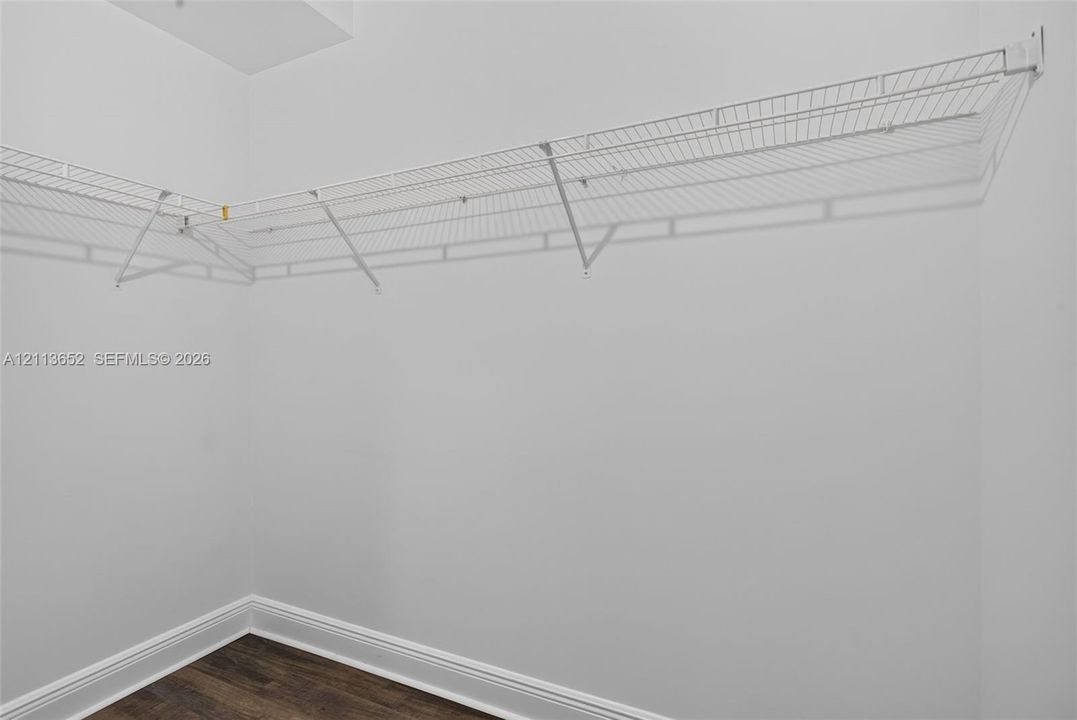 White wire-mesh shelving unit with wall-mounted brackets and wood-finish flooring