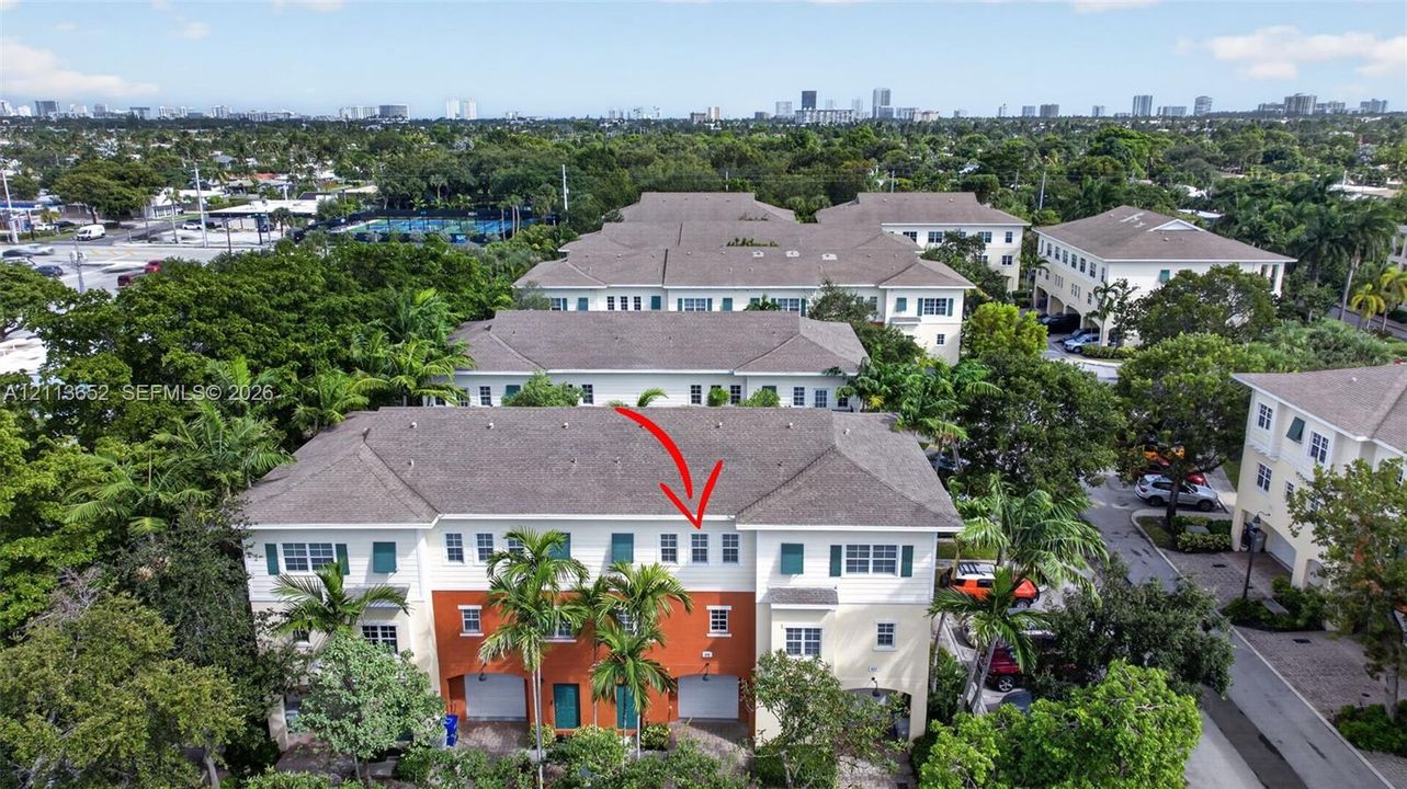 Multi-story townhouse exterior featuring a high-contrast stucco facade, attached garage, shingled hip roof, and surrounding mature landscaping