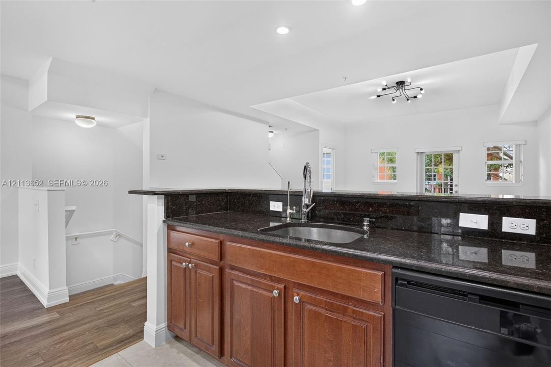 Kitchen featuring dark stone countertops, wood-finish cabinetry, stainless steel sink with high-arc faucet, integrated dishwasher, and wood-finish flooring