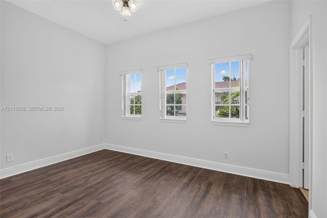 Interior room featuring wood-finish flooring, three double-hung windows, and a flush-mount light fixture