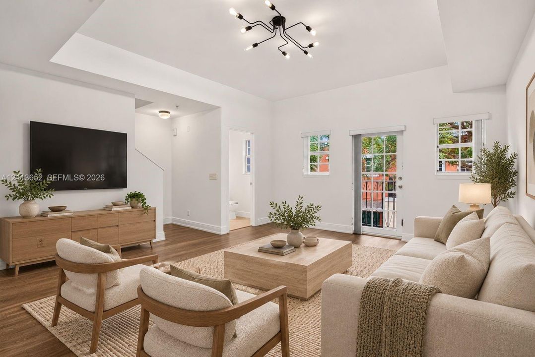 Living area featuring a tray ceiling, wood-finish flooring, multi-arm sputnik lighting fixture, and a glass-paneled exterior door