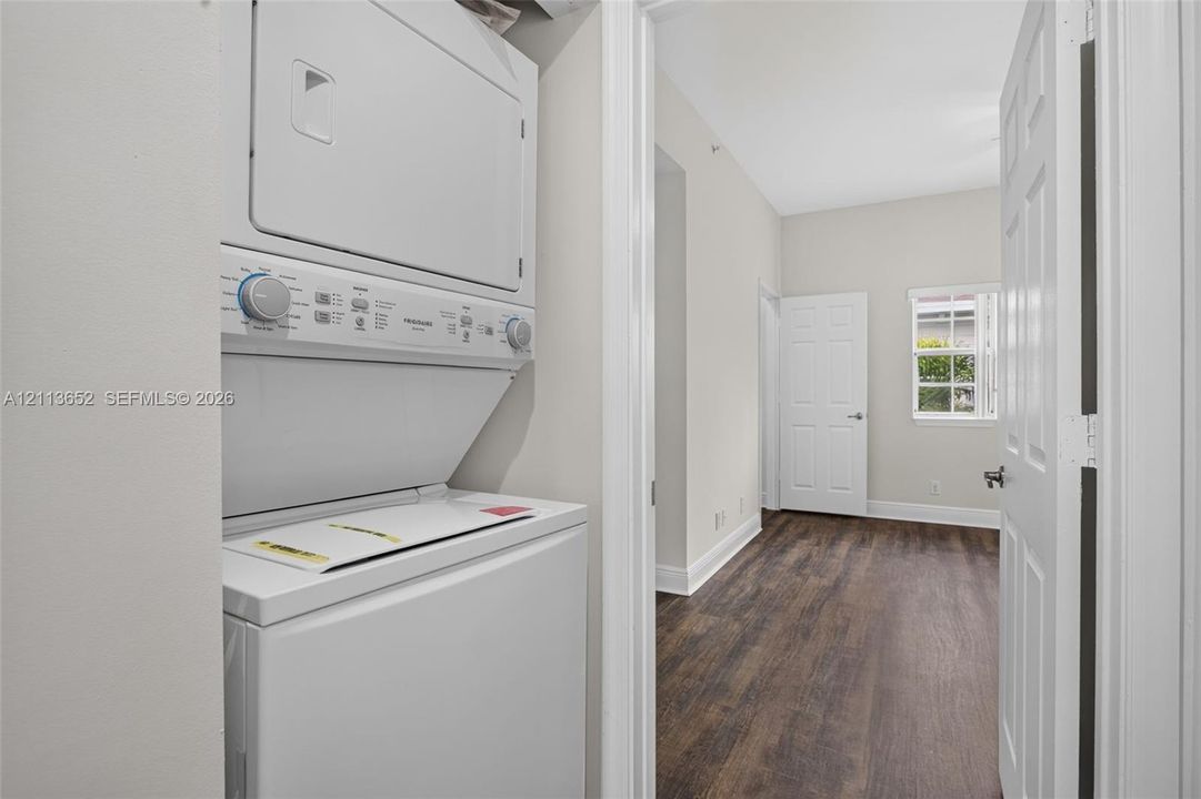 Stacked laundry appliance, wood-finish flooring, white panel doors, and a single-pane window