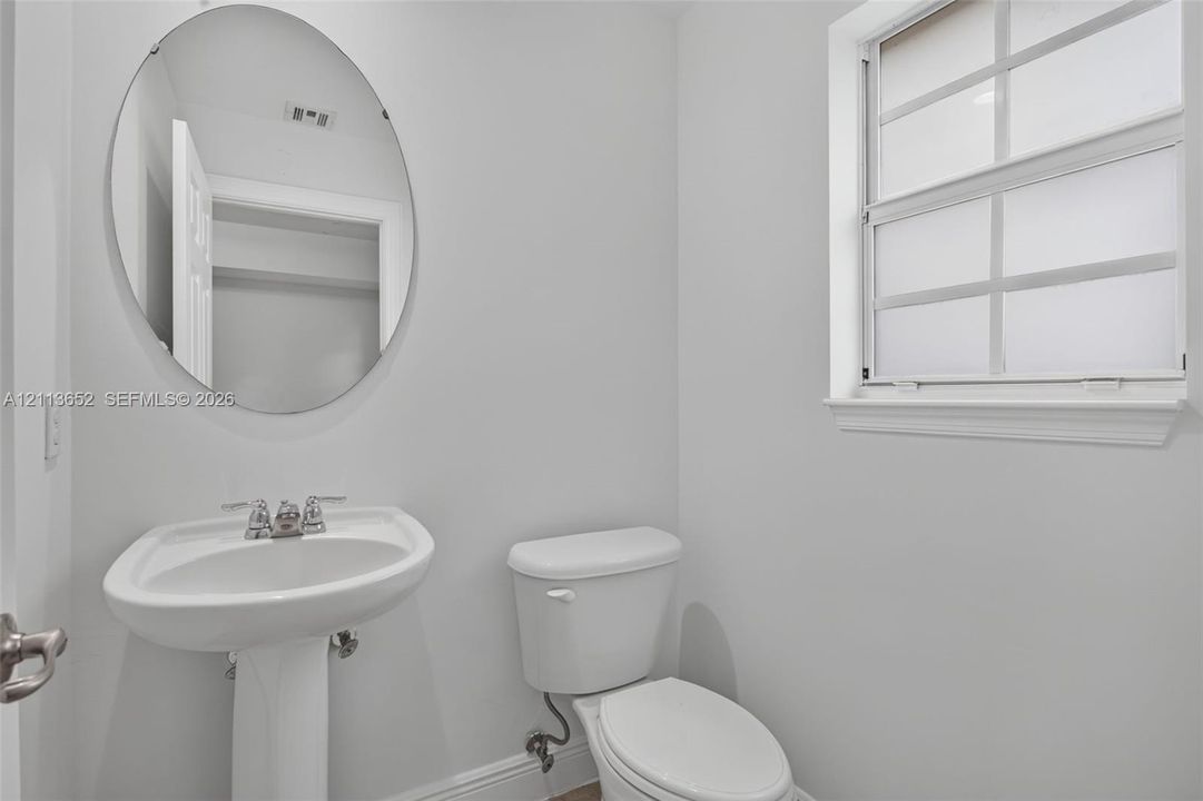 White pedestal sink with chrome faucet, oval frameless mirror, and multi-pane window with interior muntins
