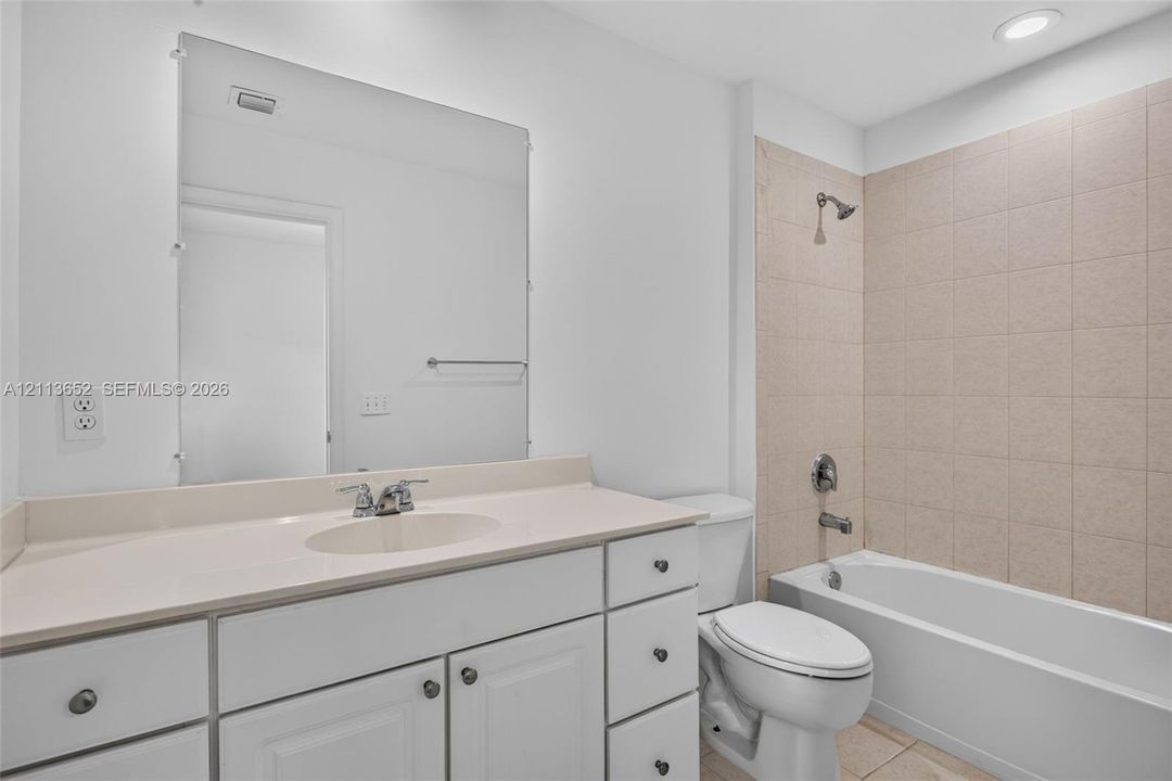 Bathroom featuring a white vanity with integrated basin, expansive wall-mounted mirror, recessed lighting, and a bathtub with tile surround
