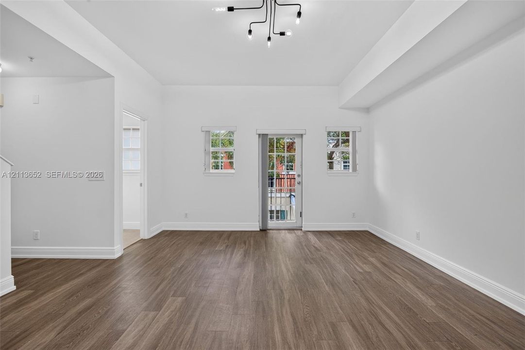 Interior space featuring high ceilings, wood-finish flooring, a multi-light modern chandelier, and a glass-paneled exterior door flanked by windows