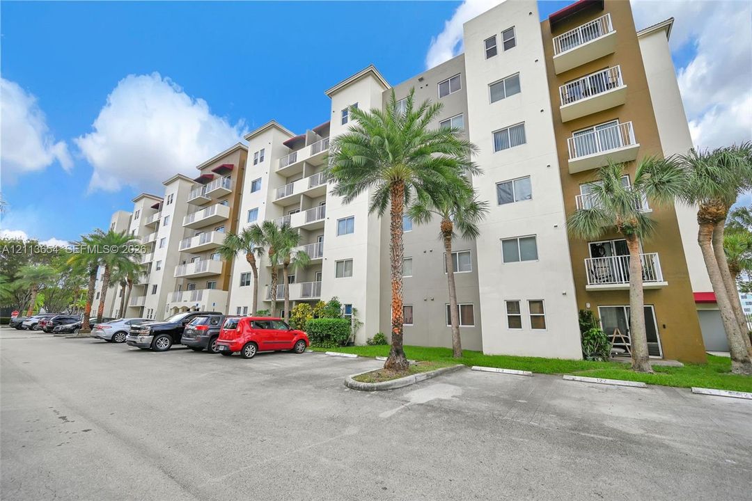 Multi-story residential building featuring a concrete exterior, private balconies, and surface parking