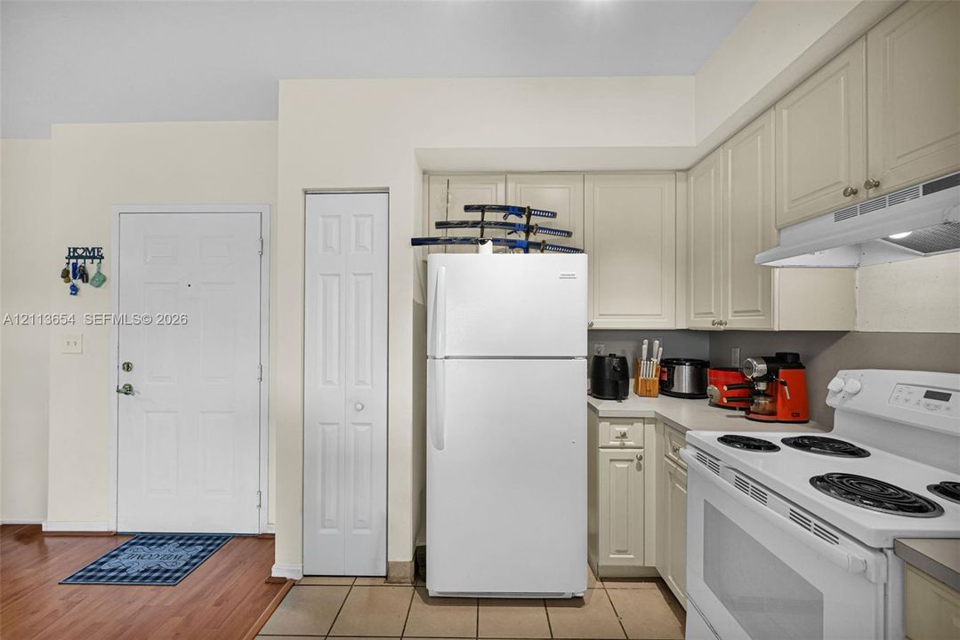 Kitchen featuring raised-panel off-white cabinetry, solid-surface countertops, white range, and white refrigerator, with wood-finish flooring in the entryway
