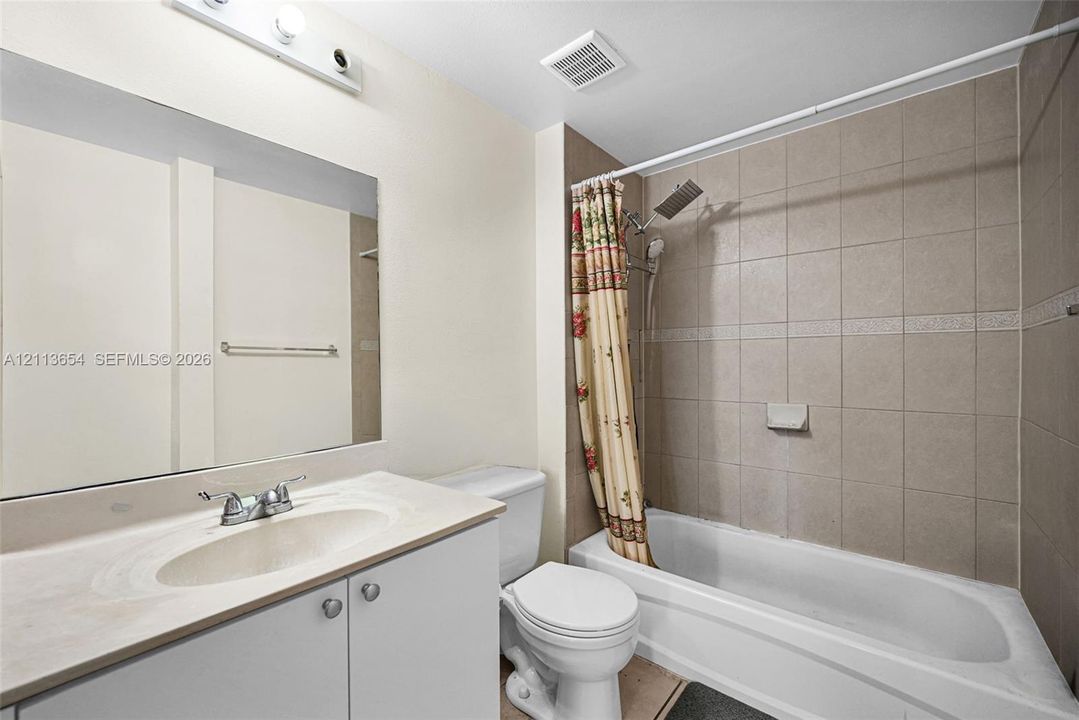 Bathroom featuring a vanity with integrated sink and countertop, large wall-mounted mirror, tub-shower combination with ceramic tile surround, and chrome-finish hardware
