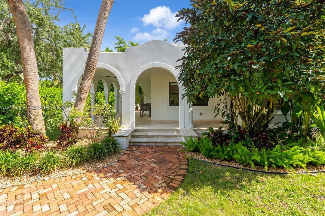 Mission-style exterior featuring a stucco facade, arched covered porch, decorative columns, and a herringbone-pattern brick walkway