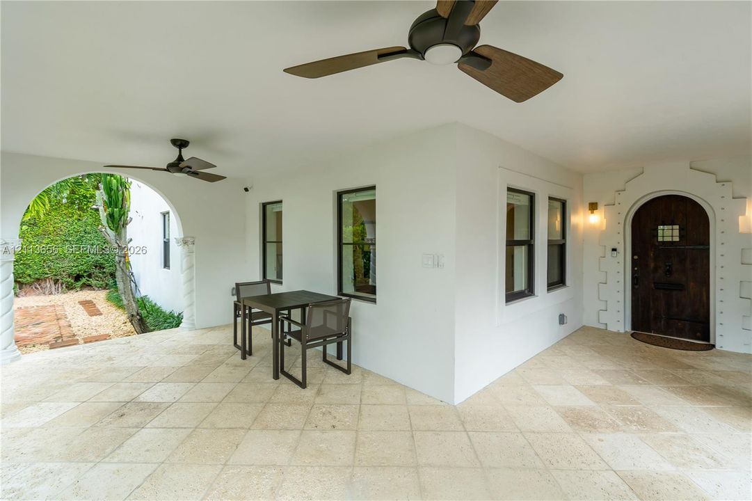 Covered patio featuring stone tile flooring, dual ceiling fans, a decorative arched entryway, and a textured stone-surround dark wood front door